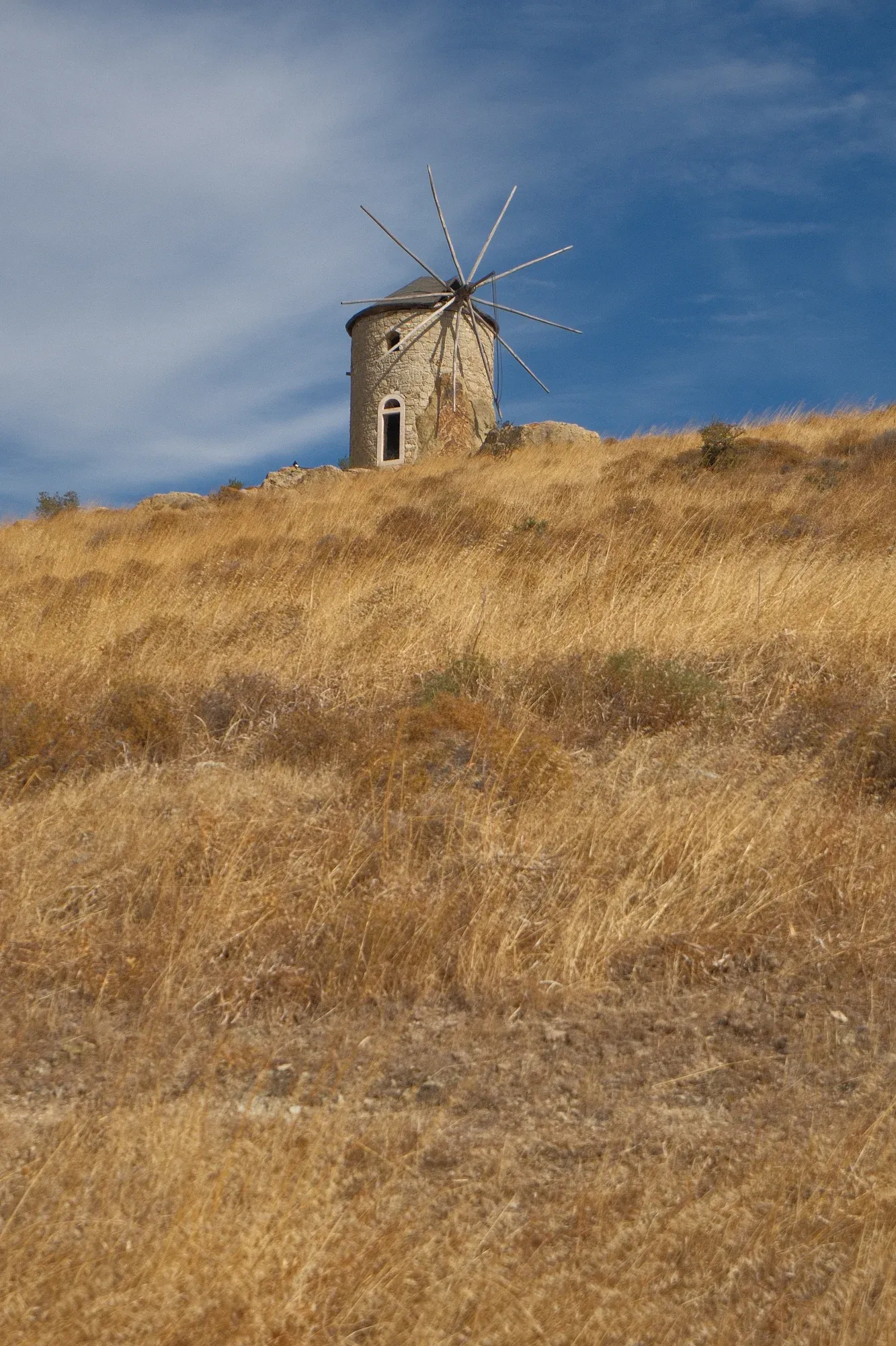 A stone windmill on a dry grassy hillside in Foça