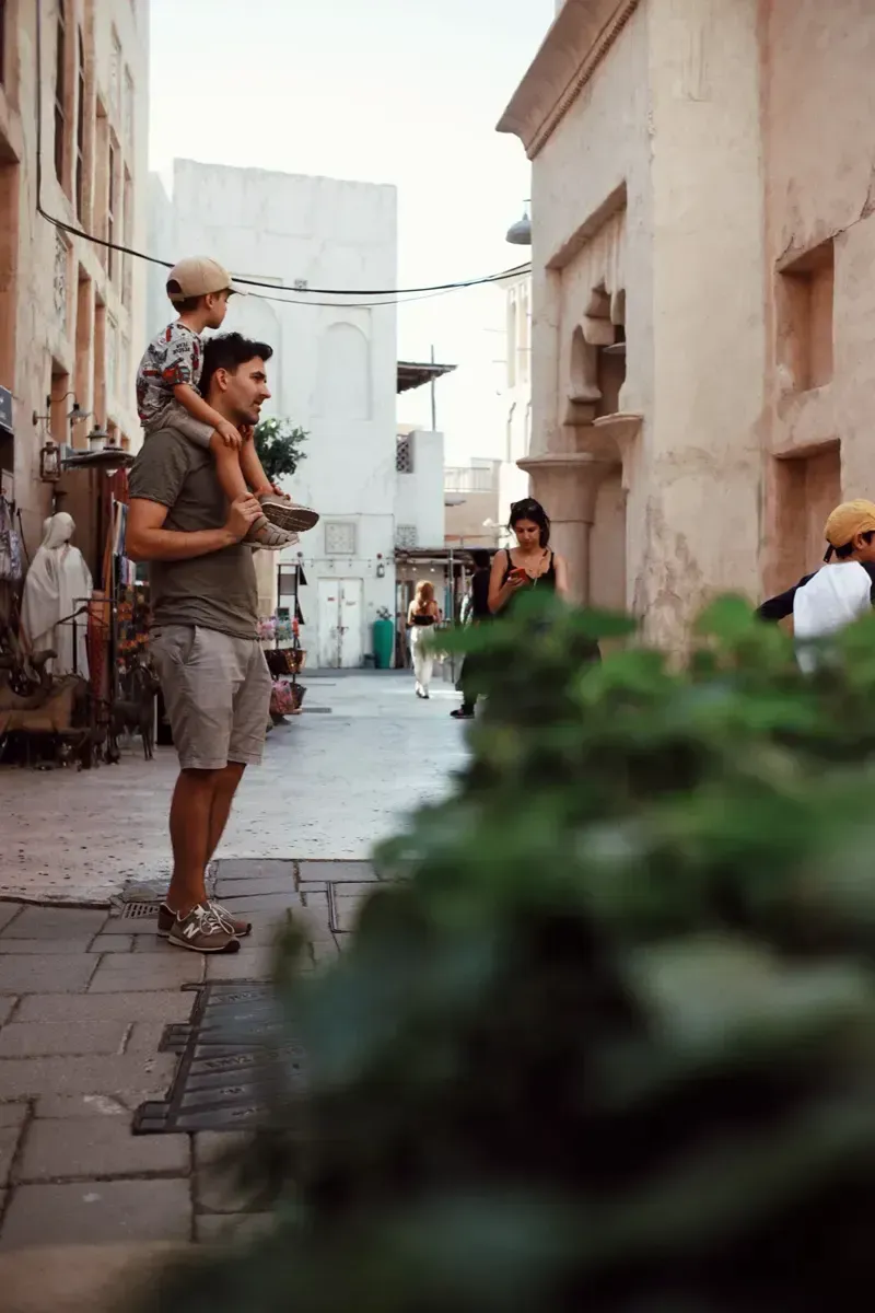 Narrow historic street with a man carrying a child on his shoulders. Photo by Kiran Johns