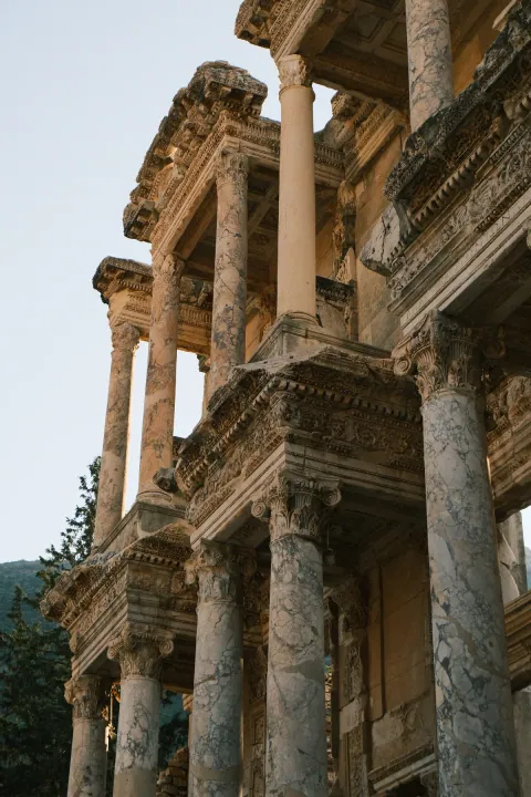 Tall veined marble columns and intricately carved stonework on an ancient facade, viewed from below.