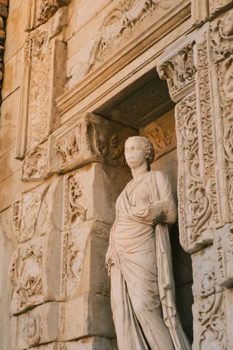 A draped classical statue stands in a stone niche surrounded by ornate floral carvings.