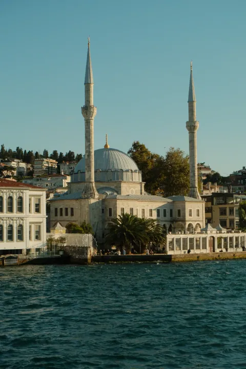 A waterfront mosque with twin minarets and a domed roof above the blue water in Istanbul.
