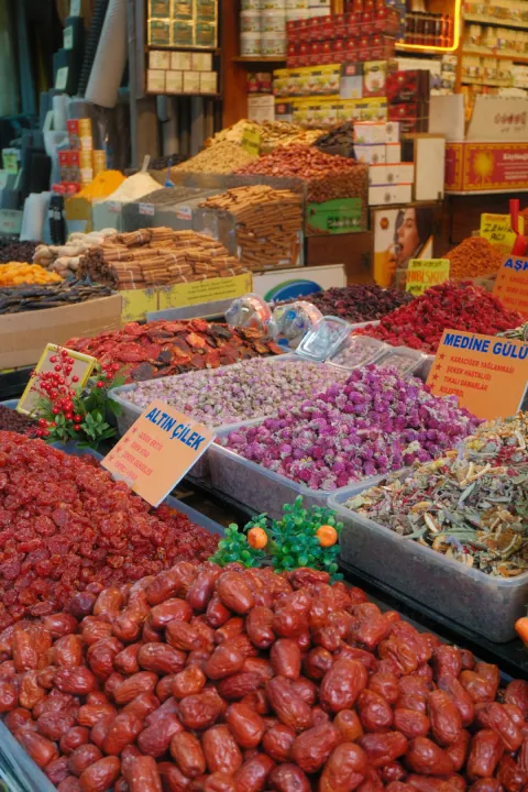 Open market trays filled with dried fruit, spices and rosebuds beneath shelves of colourful boxes.