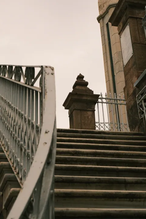 Worn stone steps lead past pale decorative iron railings beside an old stone building.